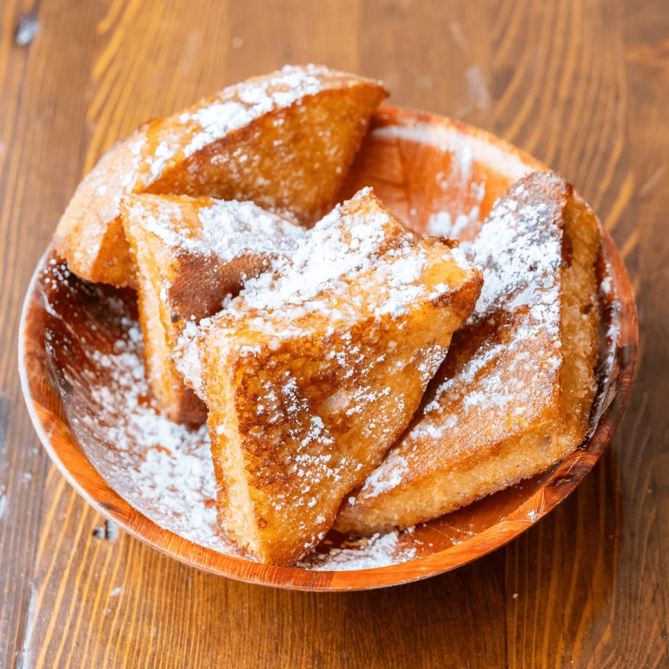Golden-brown French toast triangles, dusted with powdered sugar, in a wooden bowl on a rustic table.