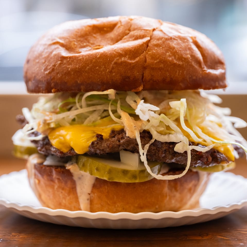Close-up of a double cheeseburger with shredded lettuce, pickles, and special sauce on a white plate.