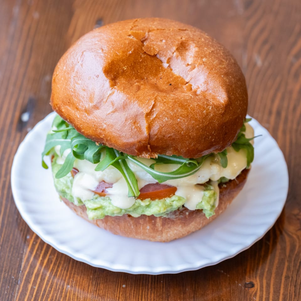 Iggy's Eggies sandwich with egg, avocado, arugula, and sauce on a white plate.
