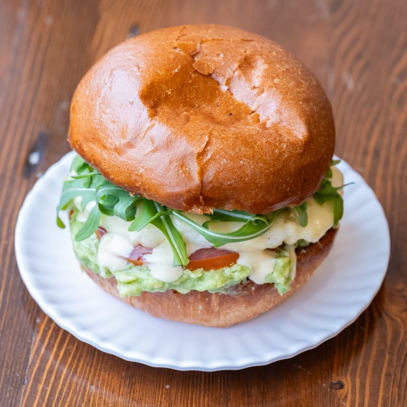 Iggy's Eggies sandwich with egg, avocado, arugula, and sauce on a white plate.