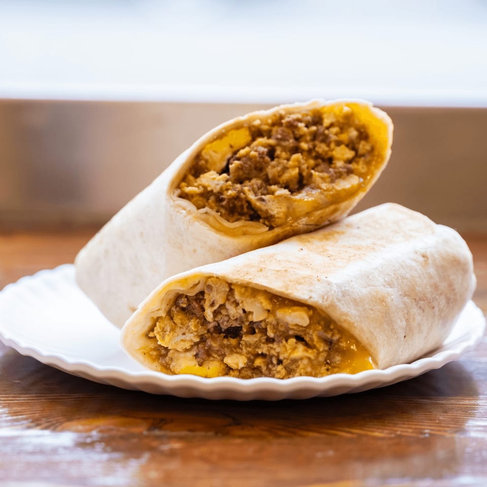 Two Iggy's Eggies breakfast burritos, filled with eggs and sausage, on a white plate.