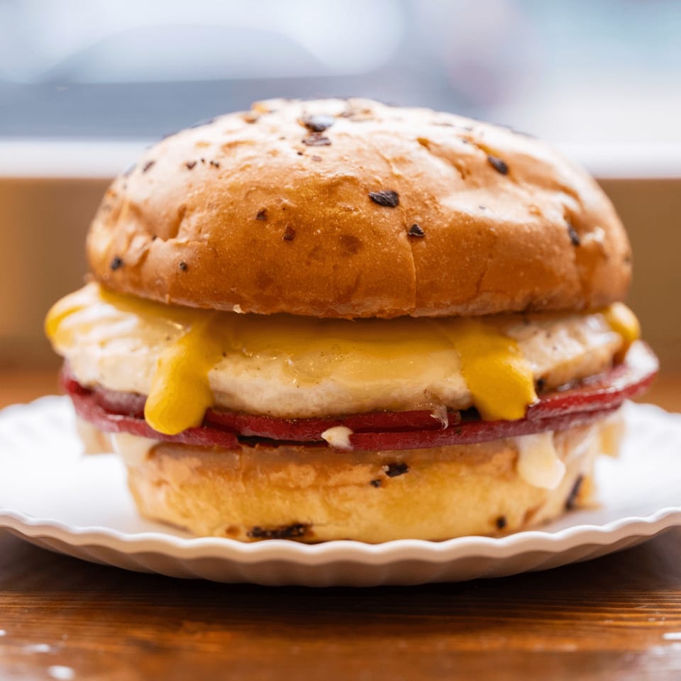 Close-up of an Iggy's Eggies sandwich with melted cheese, egg, and meat on a bun.
