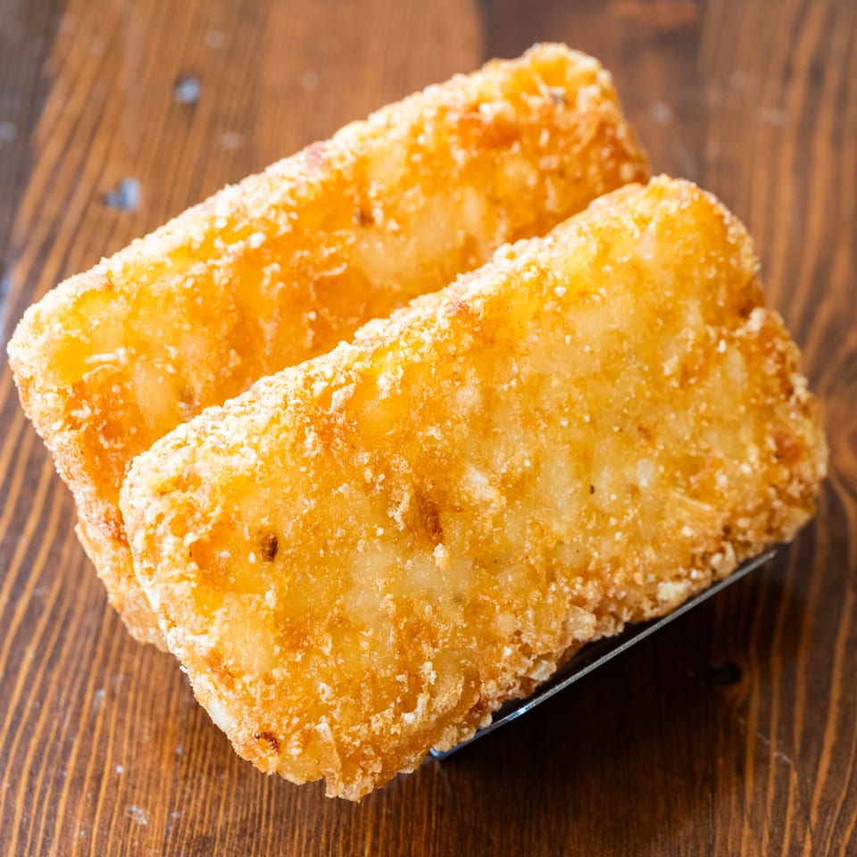 Two crispy, golden-brown hash brown patties on a dark wooden surface.