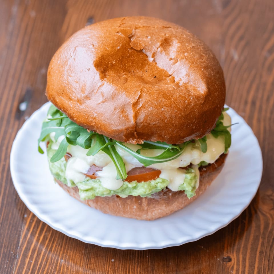 Iggy's Eggies sandwich with avocado, tomato, arugula, and creamy sauce on a white plate.