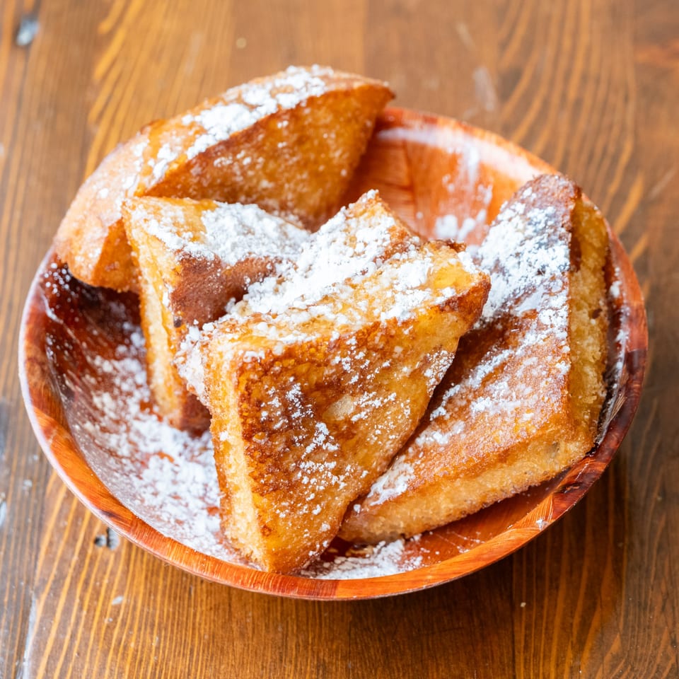 Golden French toast triangles, dusted with powdered sugar, in a rustic wooden bowl on a wood table.